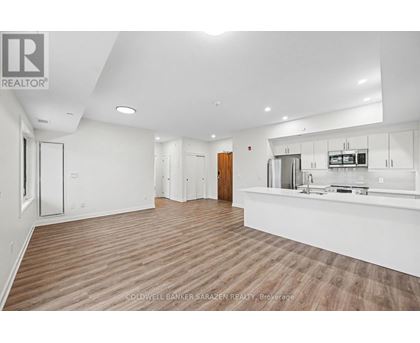 A spacious kitchen and living room with wood flooring and white walls.