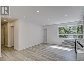 A spacious, empty room with wood flooring and a large window overlooking a forest.