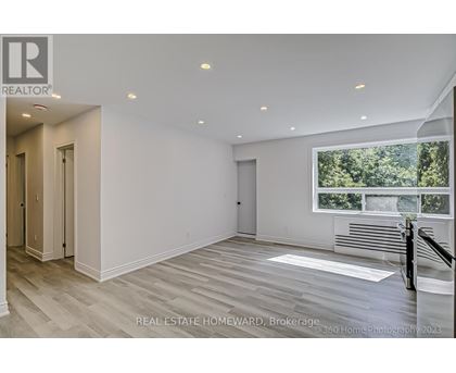 A spacious, empty room with wood flooring and a large window overlooking a forest.