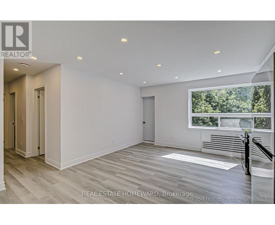 A spacious, empty room with wood flooring and a large window overlooking a forest.