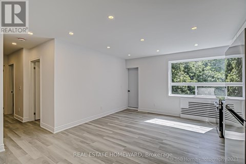 A spacious, empty room with wood flooring and a large window overlooking a forest.