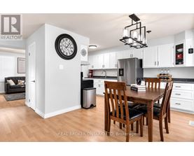 A kitchen with a table and chairs in the foreground and a clock on the wall in the background.