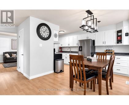 A kitchen with a table and chairs in the foreground and a clock on the wall in the background.
