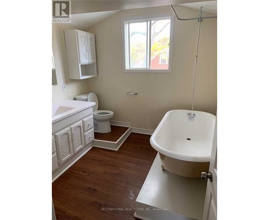 A white bathroom with wood floors and a claw foot tub.