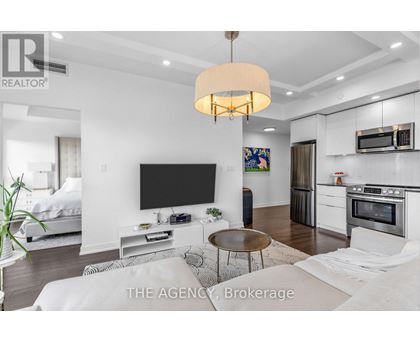 A modern living room with a flat screen TV and a kitchen area in the background.
