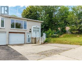A house with a white garage door and a grey door is surrounded by greenery.