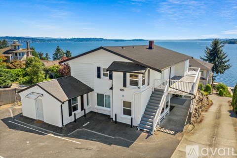 A white house with a black roof is situated by a body of water.