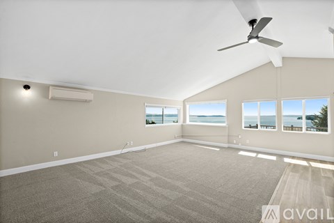 A spacious room with a ceiling fan and large windows overlooking the water.