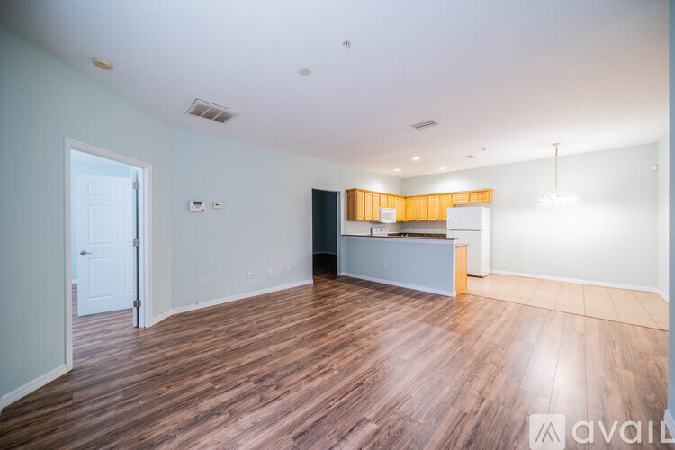 A room with wooden flooring and a kitchen area in the background.