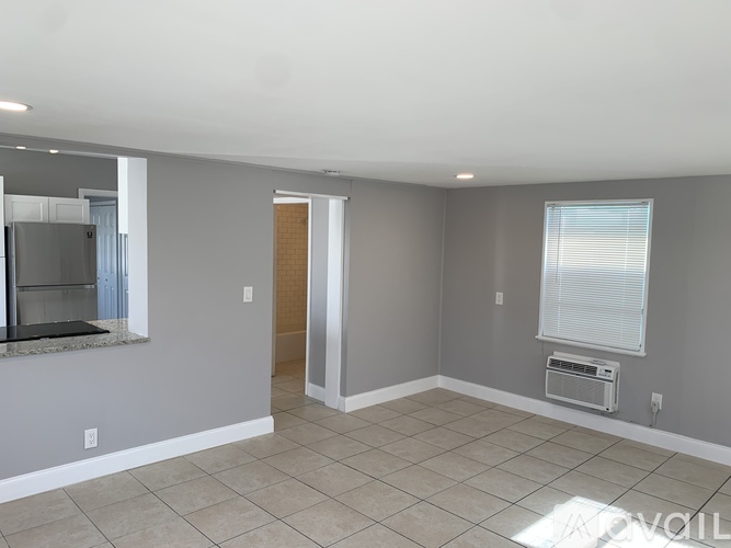 A spacious room with a doorway leading to another room, a window with blinds, and a wall-mounted air conditioning unit.