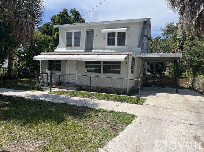 A white two-story house with a black fence and a driveway in front.