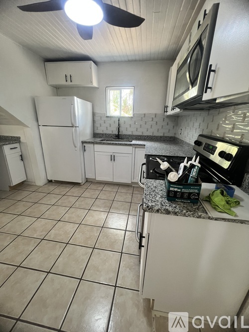 A kitchen with white appliances and a fan on the ceiling.