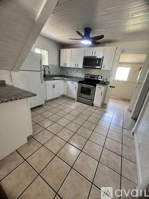 A kitchen with white cabinets and a black fan.