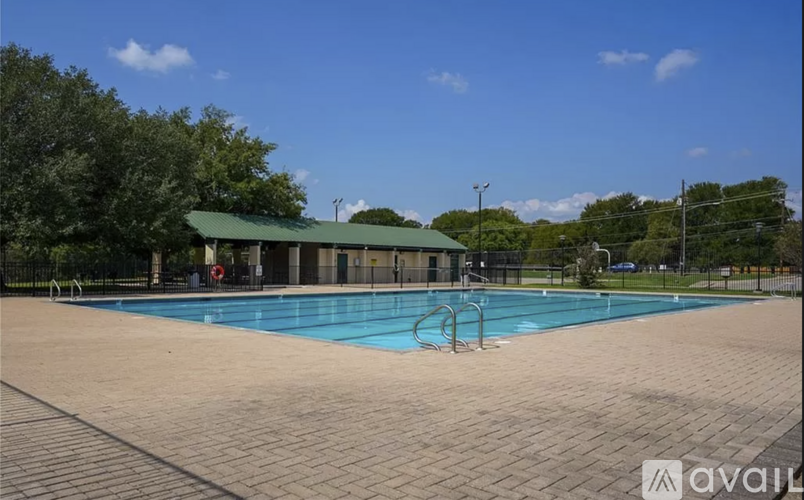A large outdoor swimming pool surrounded by a brick patio and a green roofed pavilion.