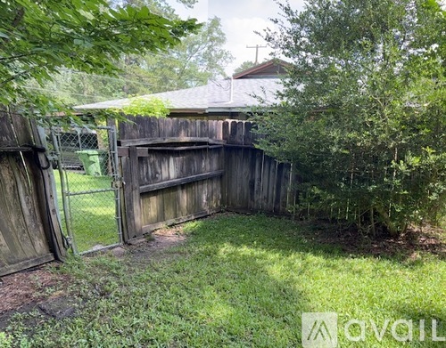 A wooden fence with a gate is partially open, surrounded by greenery.