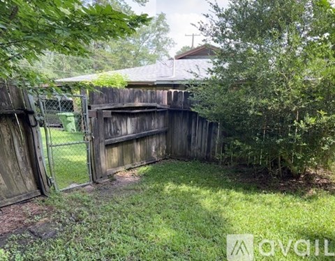 A wooden fence with a gate is partially open, surrounded by greenery.
