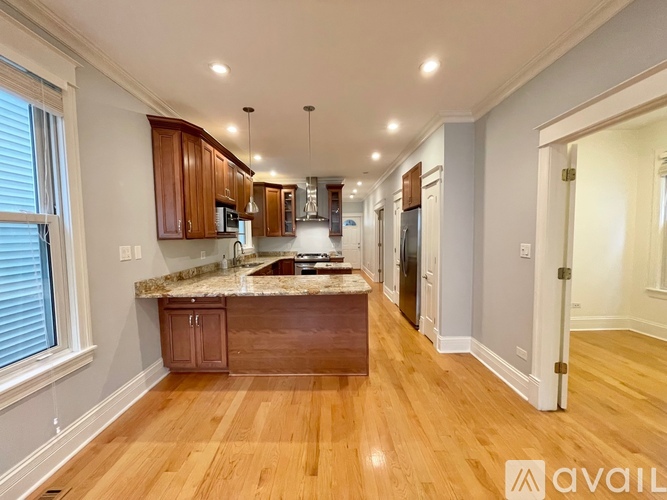 A kitchen with wooden floors and cabinets, a marble countertop, and a refrigerator.
