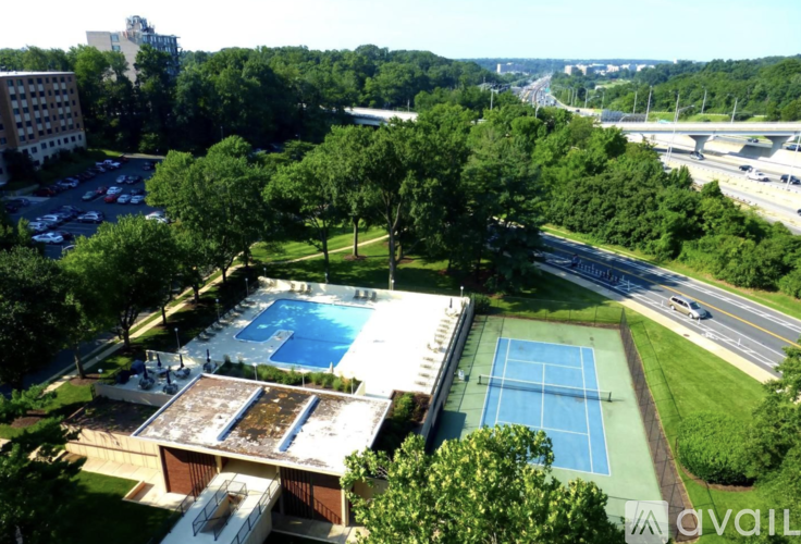 A pool and tennis court are surrounded by trees.