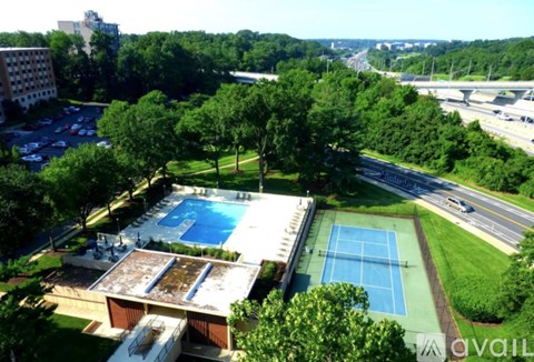 A pool and tennis court are surrounded by trees.