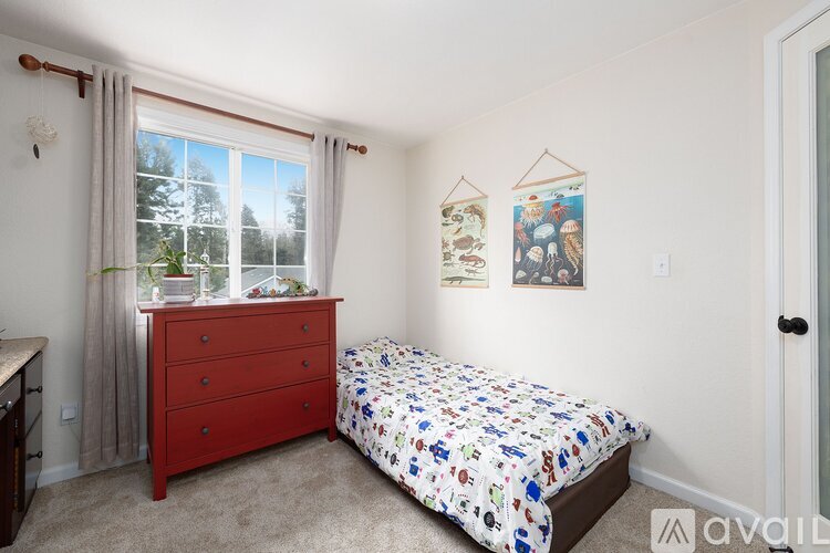 A bedroom with a red bed and a window with curtains.