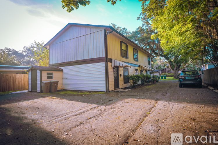 A yellow house with a garage door is surrounded by trees and has a car parked in front.