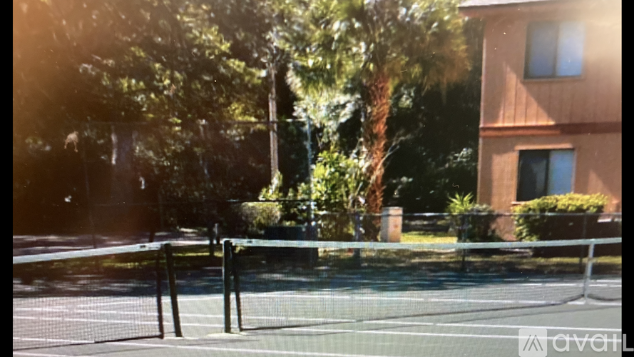 Tennis court surrounded by trees and a building.