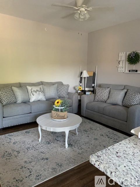 A living room with two grey couches, a coffee table with a sunflower and a sign that says "Blessed", and a ceiling fan.