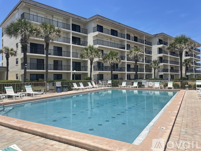 A large swimming pool is surrounded by a building with balconies and palm trees.