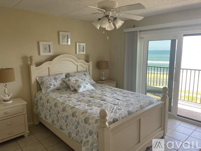 A bedroom with a large bed and a view of the ocean through a sliding glass door.