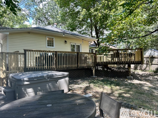 A backyard with a hot tub, wooden deck, and a tree.