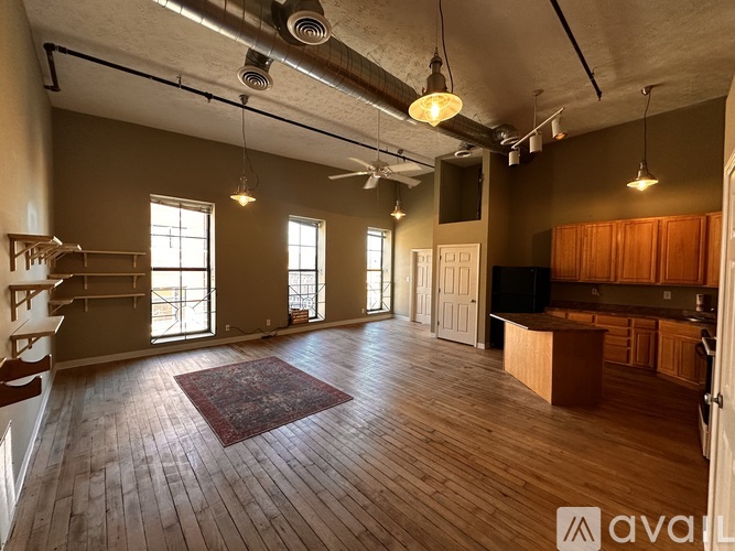 A spacious room with wooden floors and a large rug in the center.