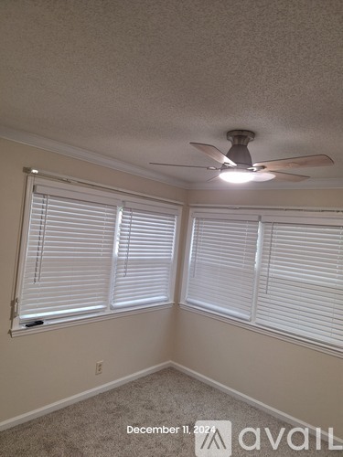 A room with a ceiling fan and two windows with blinds.