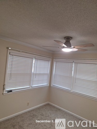 A room with a ceiling fan and two windows with blinds.