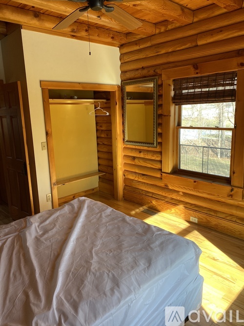 A bedroom with a bed covered in white sheets and a window with blinds.