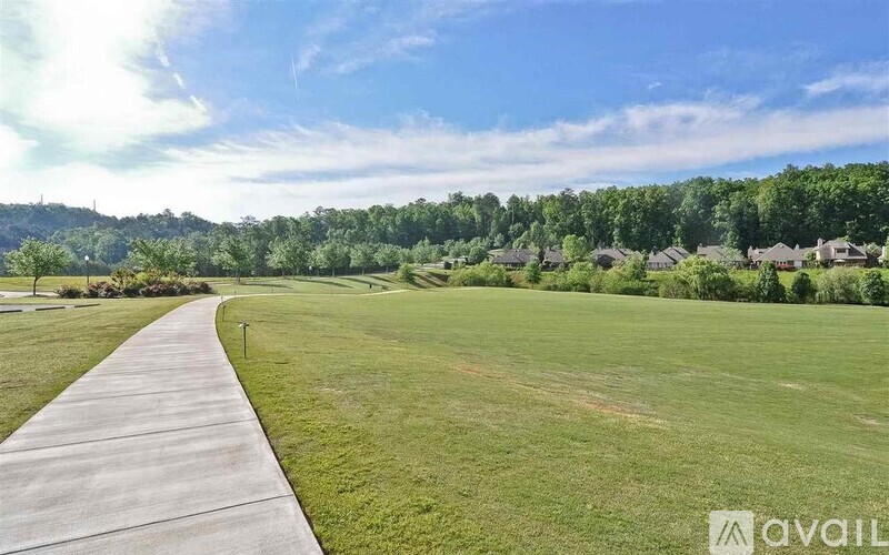 A long concrete walkway leads through a grassy field with houses in the distance.