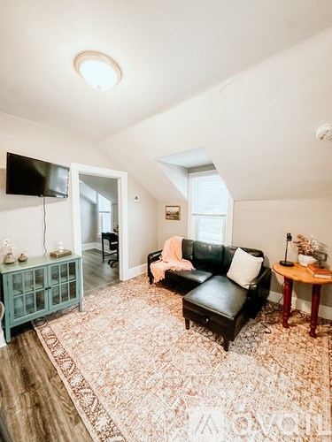 A living room with a black leather couch and a patterned rug.