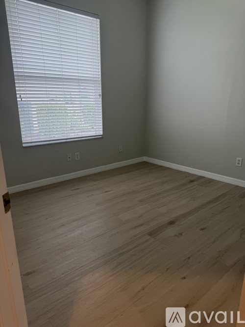 A room with a window covered by white blinds and wooden flooring.