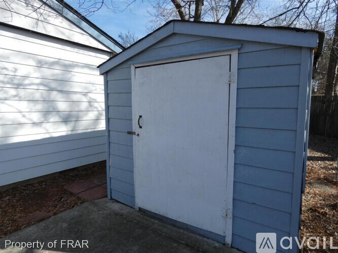 A small blue shed with a white door is situated in front of a white building.