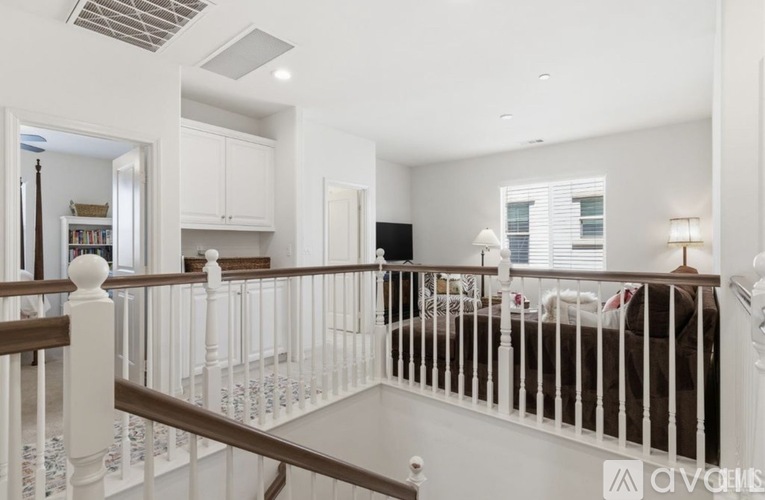 A white staircase with a railing leads to a bedroom with a bed and a window.