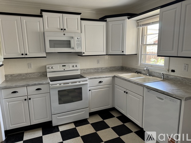 A kitchen with white cabinets and a black and white checkered floor.
