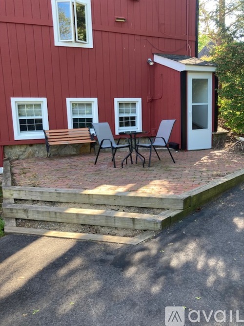 A red building with a white door and windows, a bench, and a table with chairs.