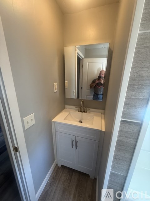 A man is taking a picture of a bathroom with a sink and mirror.