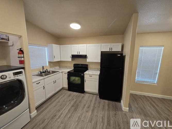 A kitchen with a black refrigerator, white cabinets, and a stove top oven.