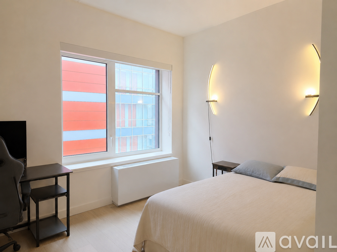 A bedroom with a bed, desk, and window.