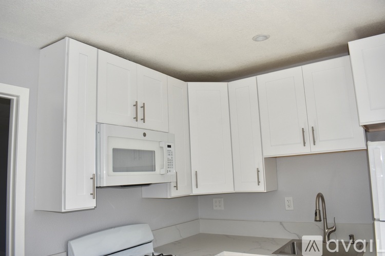 A kitchen with white cabinets and a white microwave.