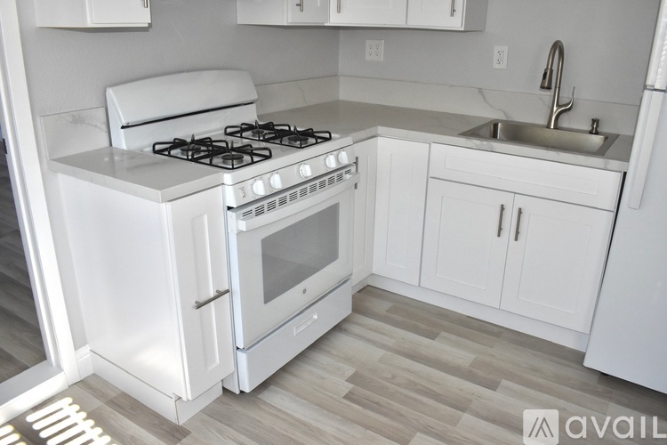 A white kitchen with a stove, sink, and cabinets.