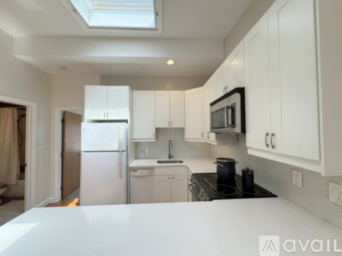 A kitchen with white cabinets and appliances, a skylight above the counter, and a dining area visible in the background.