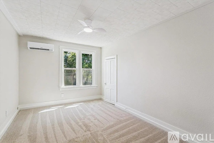 A room with a carpeted floor, a ceiling fan, and a window with a view of trees.