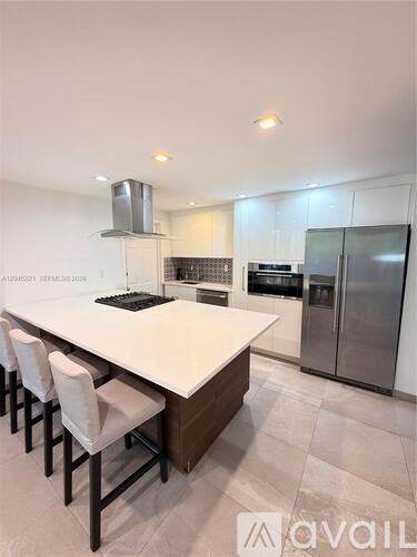 A modern kitchen with a long white island and stainless steel appliances.