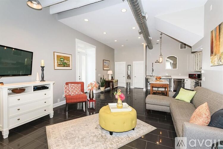 A living room with a white couch, a yellow ottoman, and a white dresser.